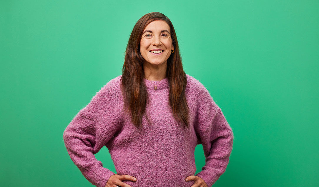 Portrait of a female employee with a pink sweater against a green background.