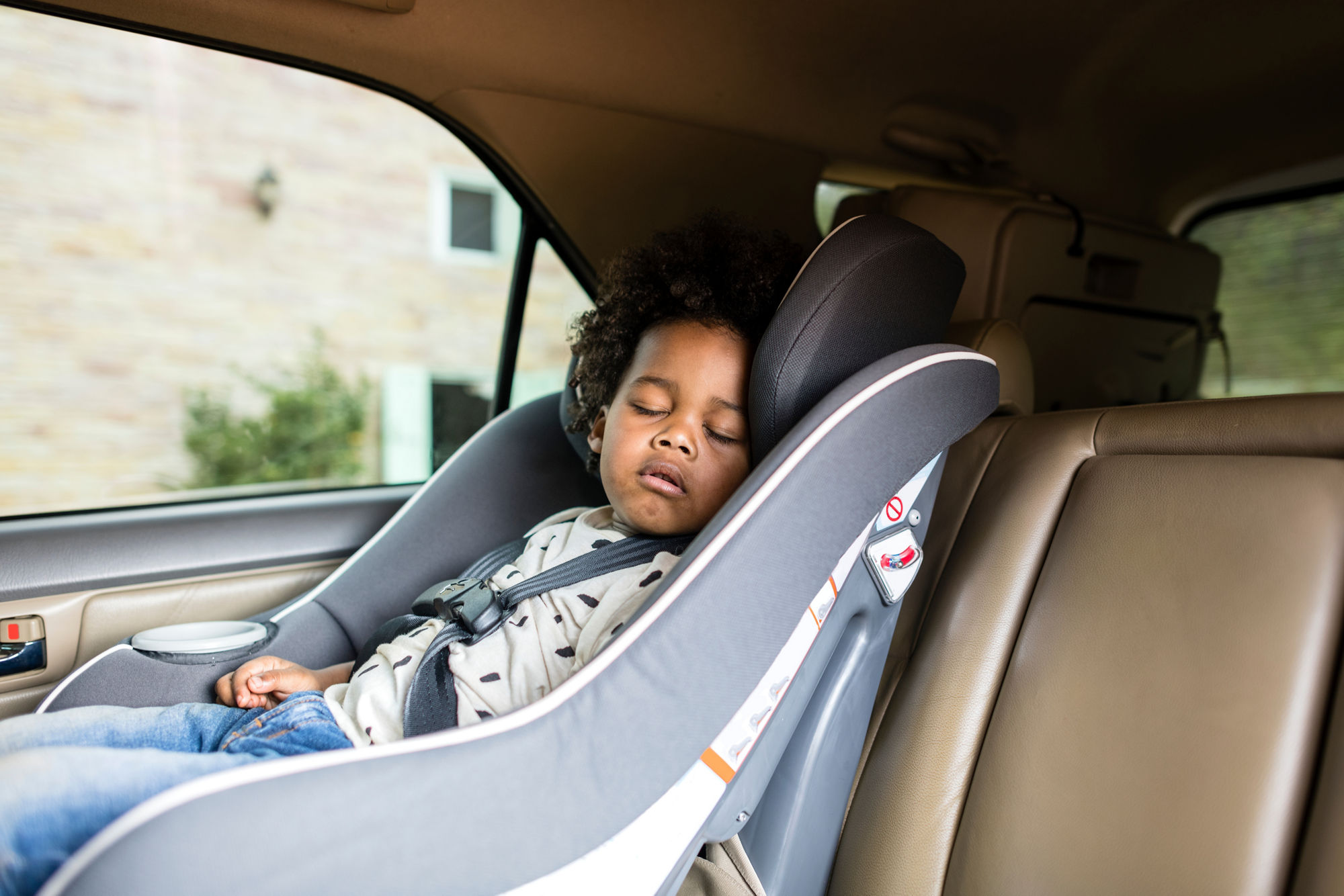 Ein Kleinkind sitzt schlafend im Kindersitz eines Autos.