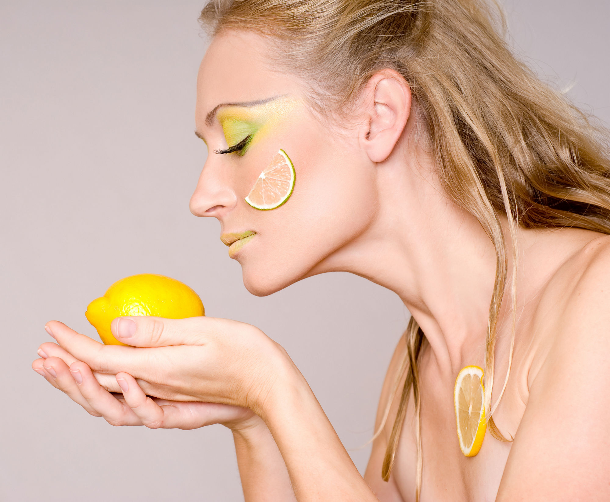 Gorgeous young woman wearing colorful make-up and holding slice of lemon