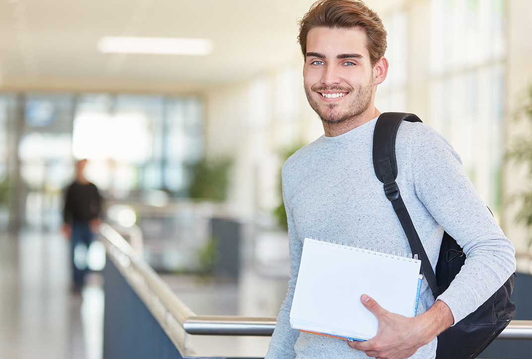 A student is standing with notebooks at the university.
