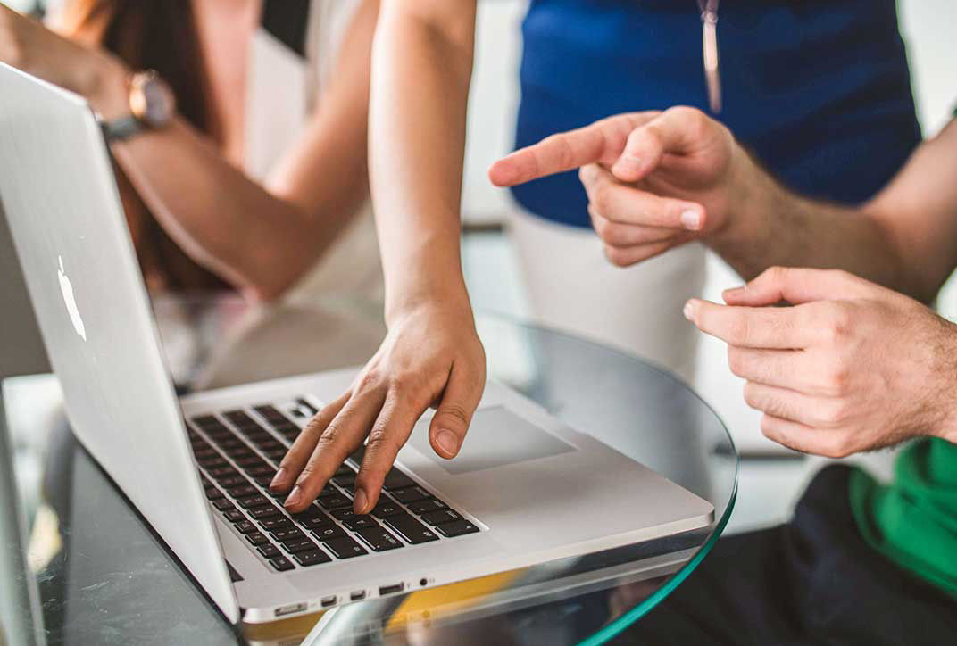 One person is explaining something to another on a laptop.