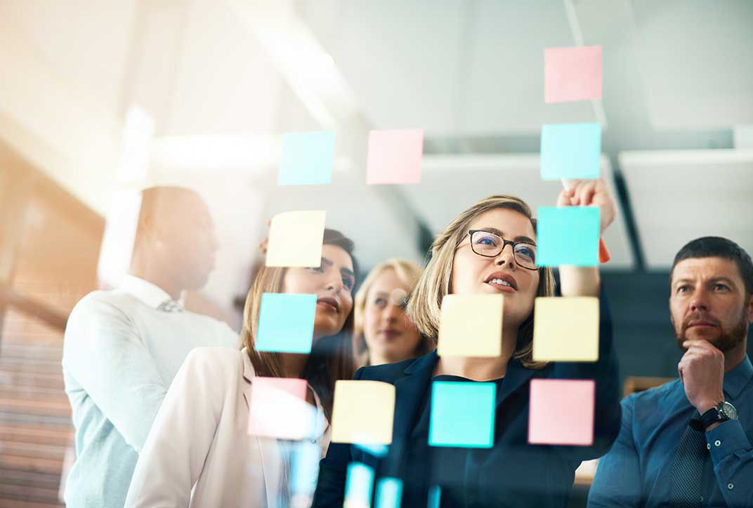 Business team at a creative brainstorming session with colorful sticky notes on a glass wall.