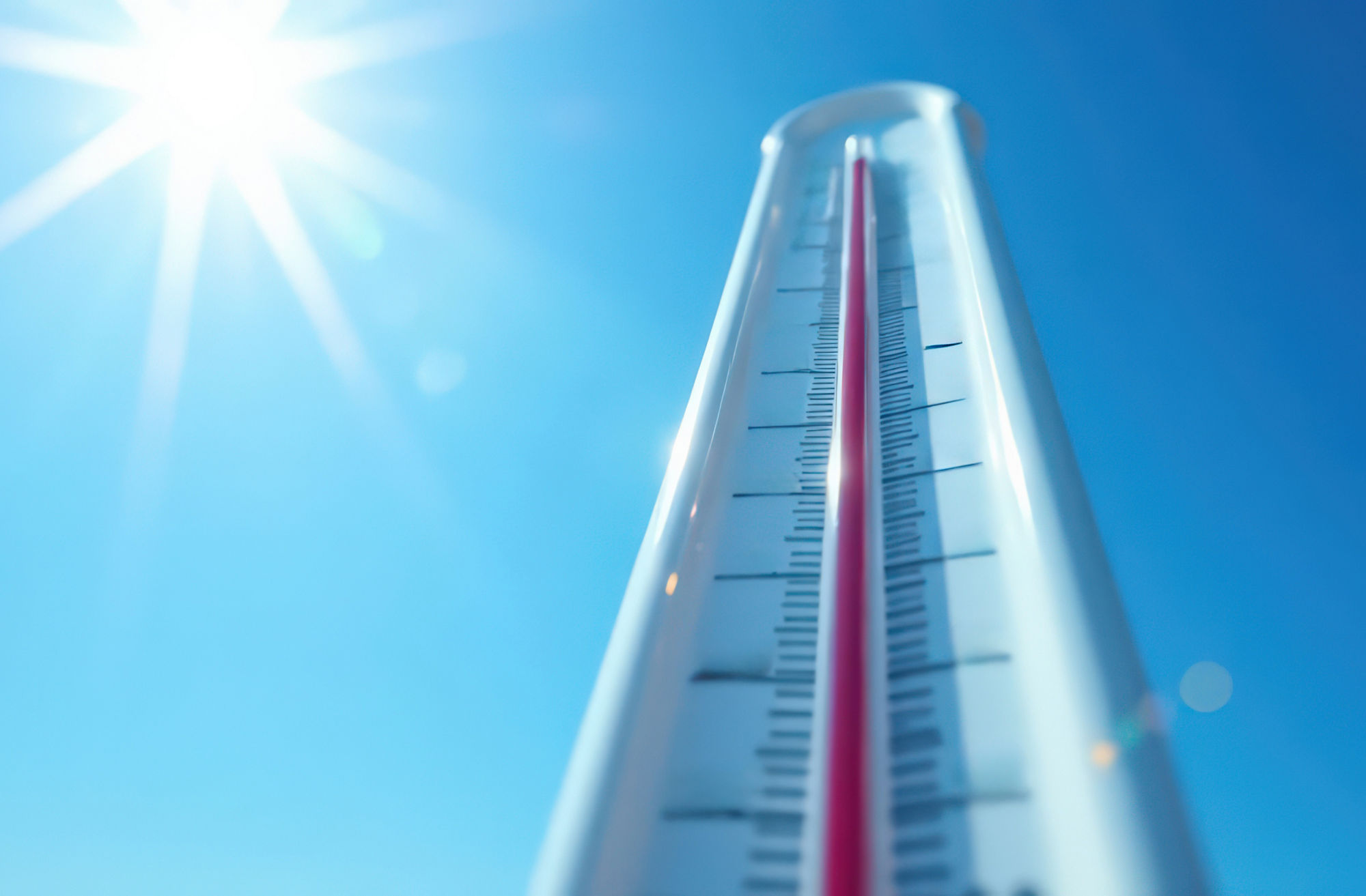 Sunny day with high temperatures captured by outdoor thermometer against clear blue sky.