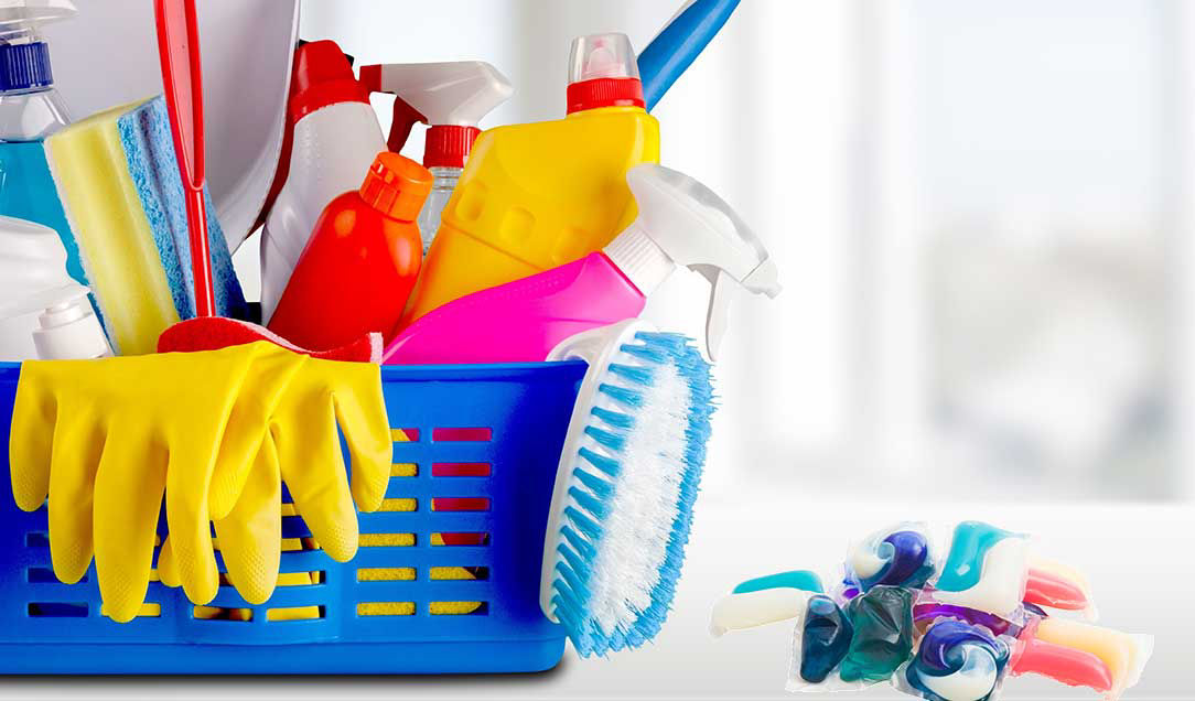 A basket containing brushes and household cleaners. Beside the basket are some laundry pods.