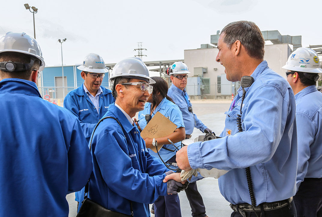 Employees and visitors greeting each other with safety helmets on the Kuraray factory site.