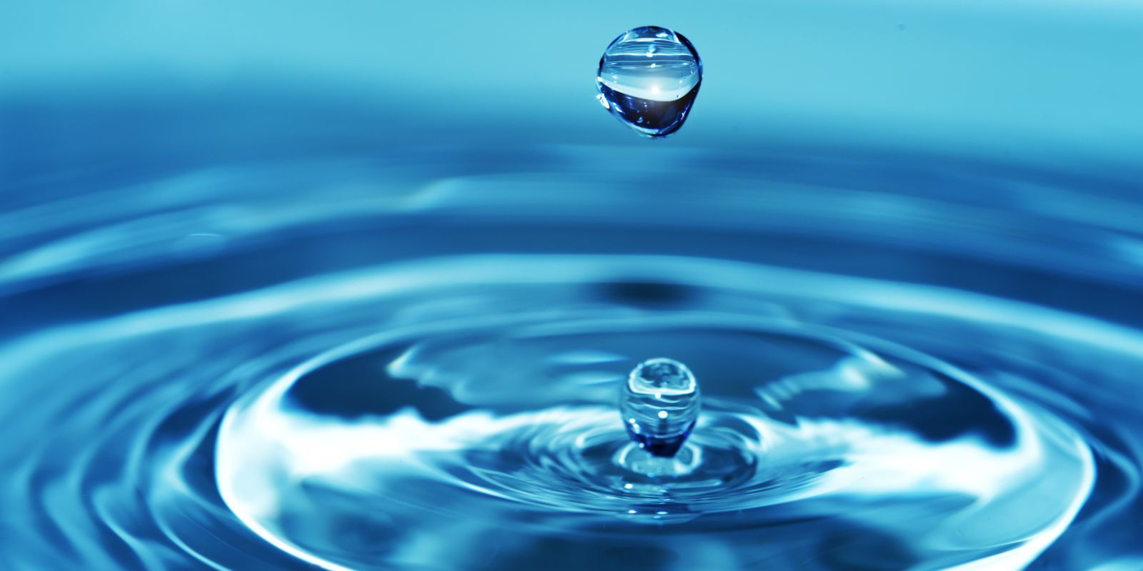 A single water droplet creating ripples on a calm blue water surface.