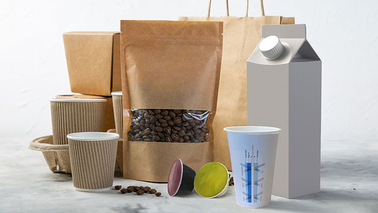 Various eco-friendly packaging items including paper bags, coffee cups, a carton container, and a pouch filled with coffee beans