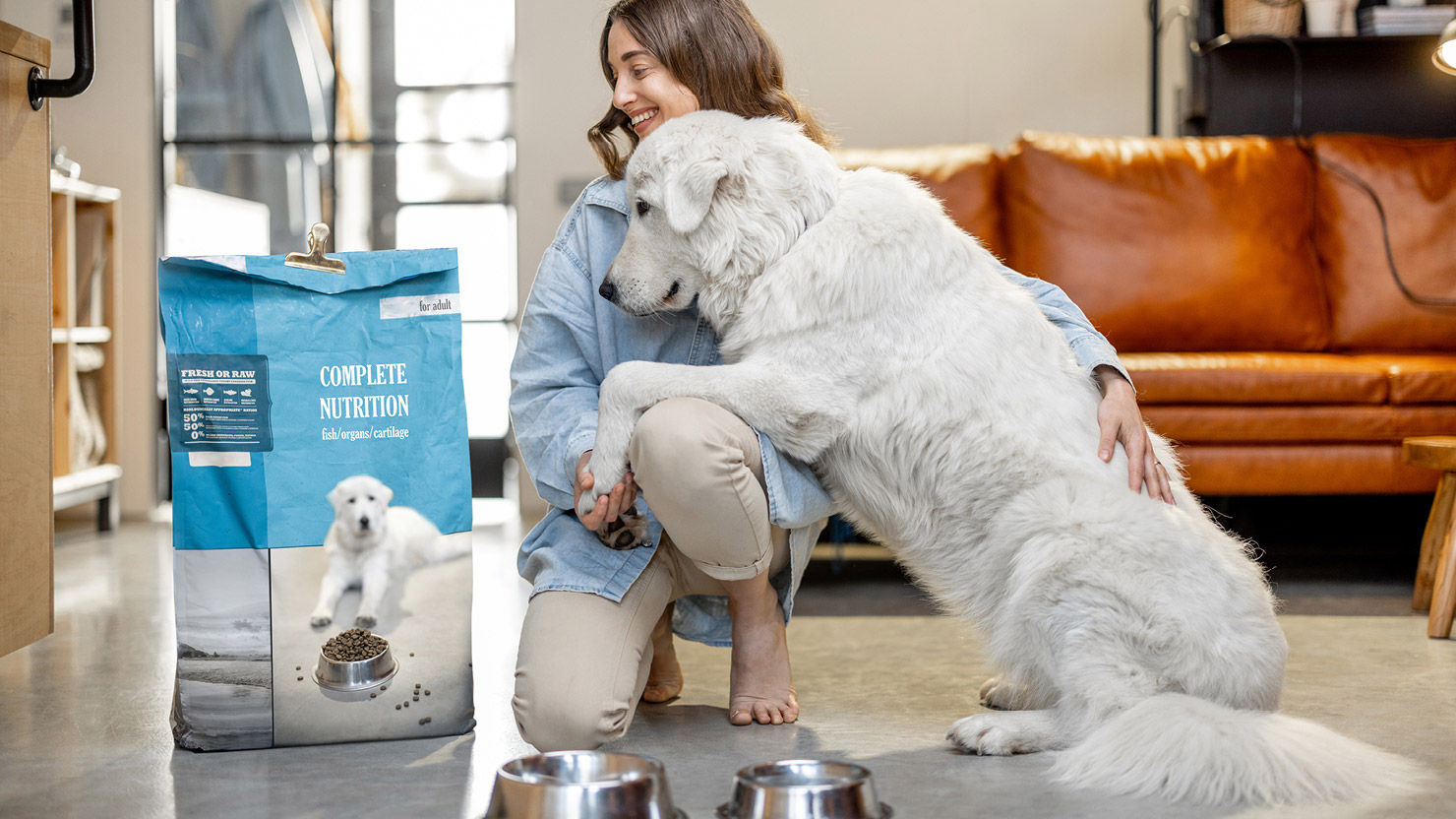 Hund und Hundebesitzer sitzen vor einer Papierverpackung, die Hundefutter enthält 