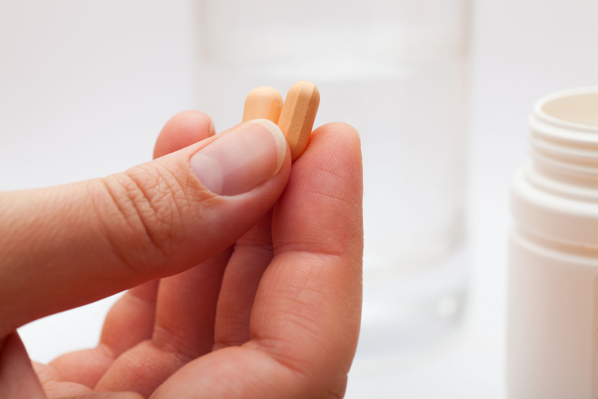 Eine Hand hält zwei orangefarbene Tabletten.