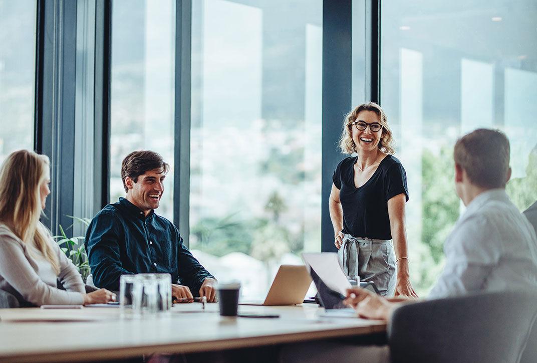 A woman stands in a meeting in front of colleagues.