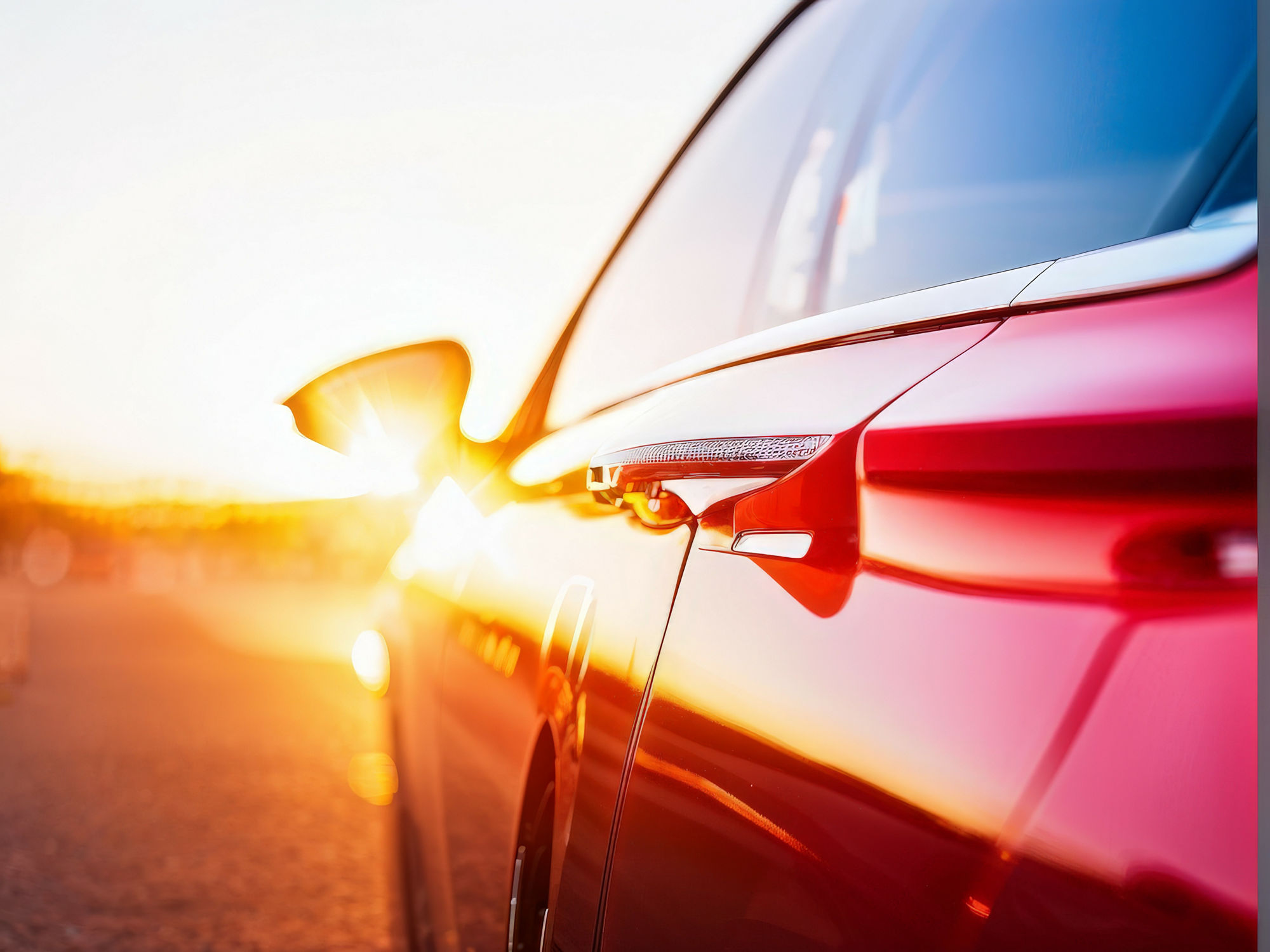 Ein Auto während der Fahrt. Man sieht es von der Seite, im Hintergrund geht die Sonne unter.