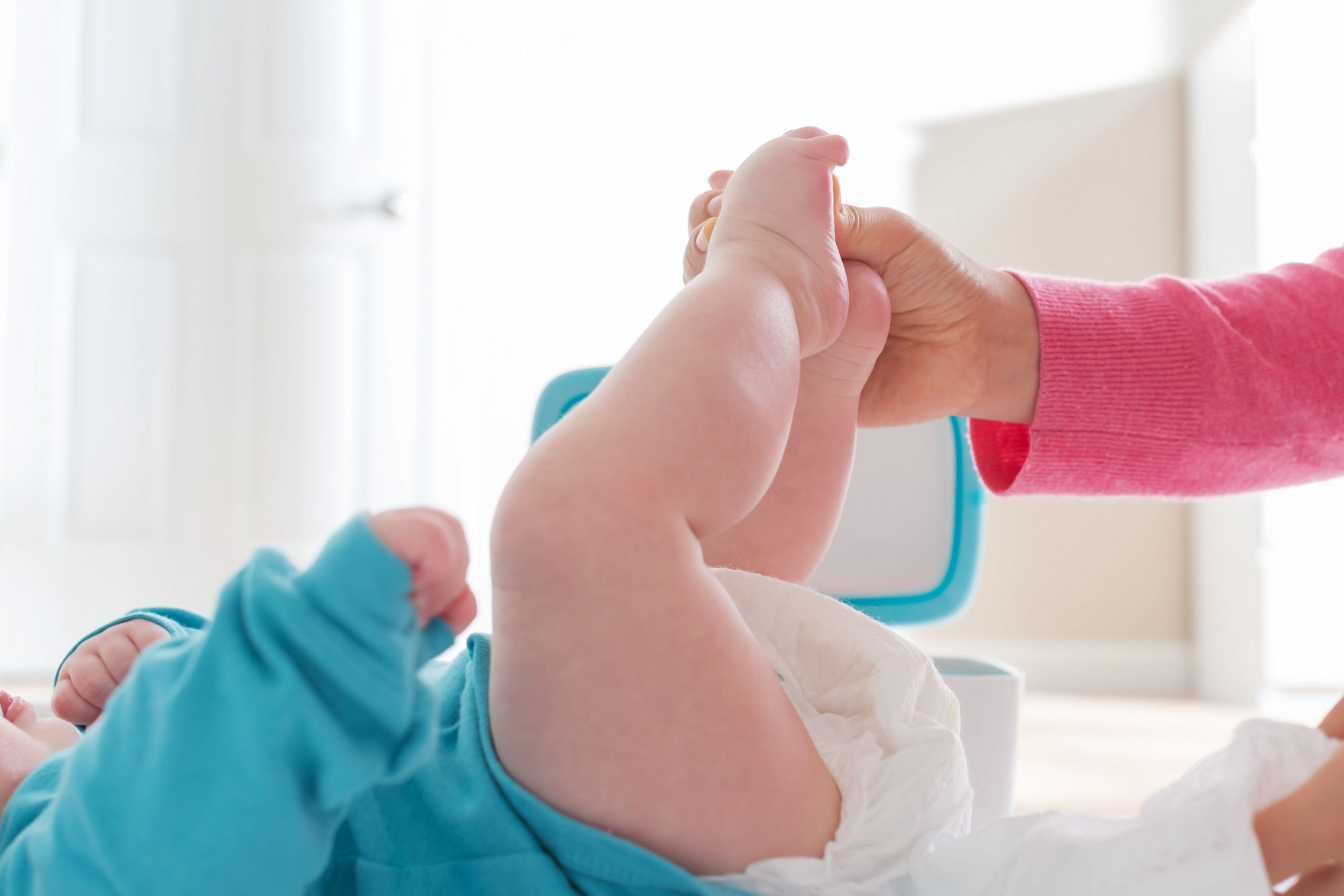 Der Unterkörper eines Babys auf einem Wickeltisch. Im Hintergrund steht ein Spender mit Feuchttüchern, daneben ist ein Stapel Windeln.