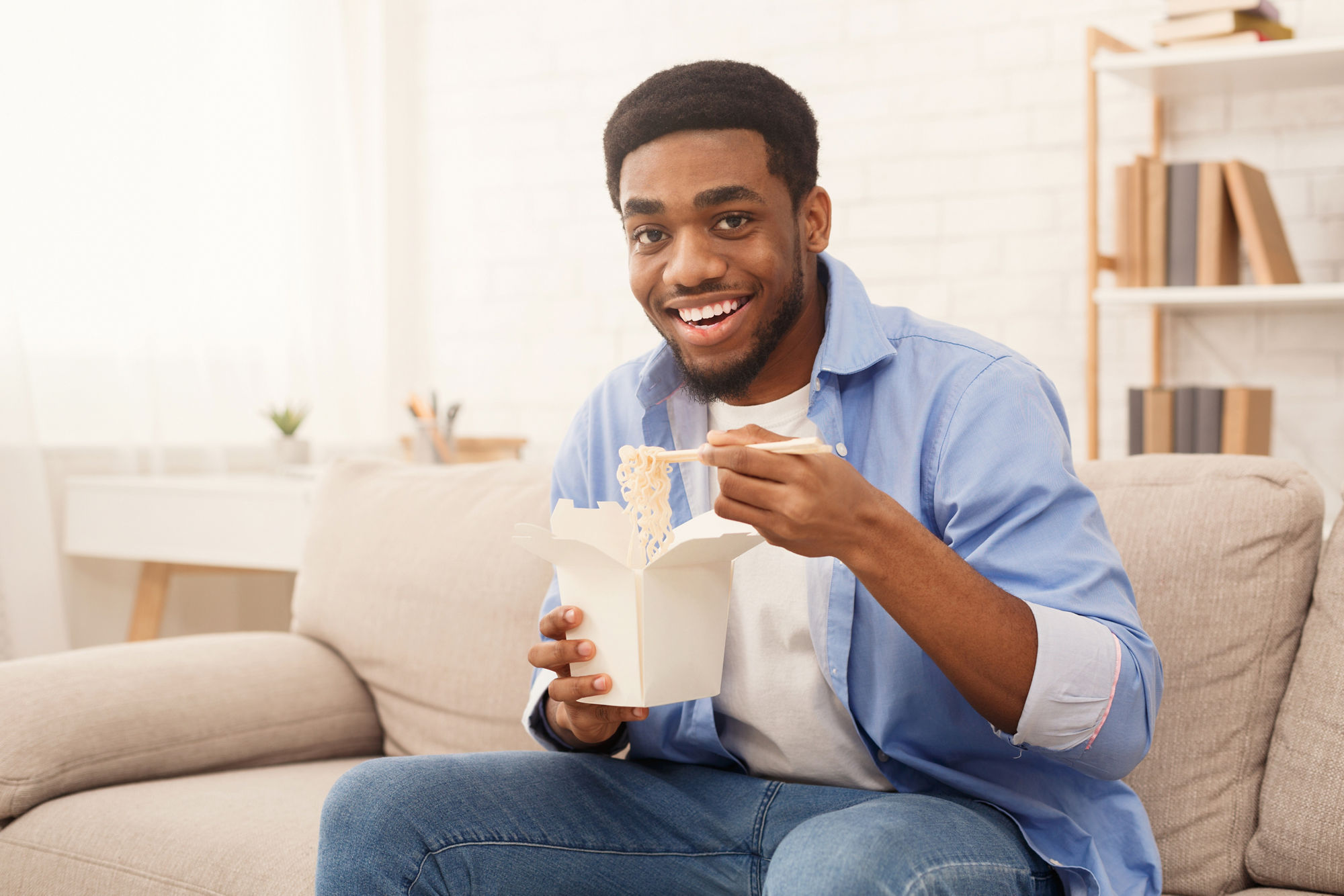 A man eating noodles from a paper box