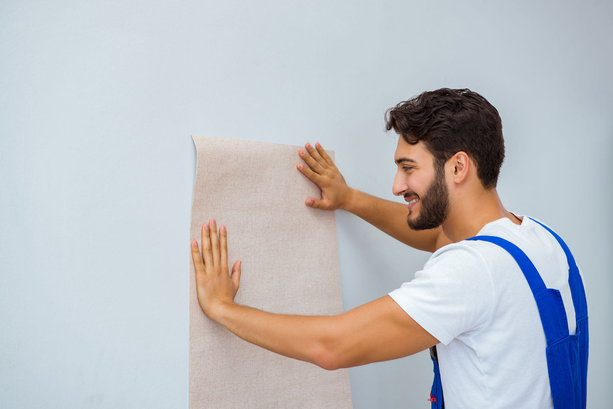 Ein Mann hält eine Tapetenbahn an eine Wand.