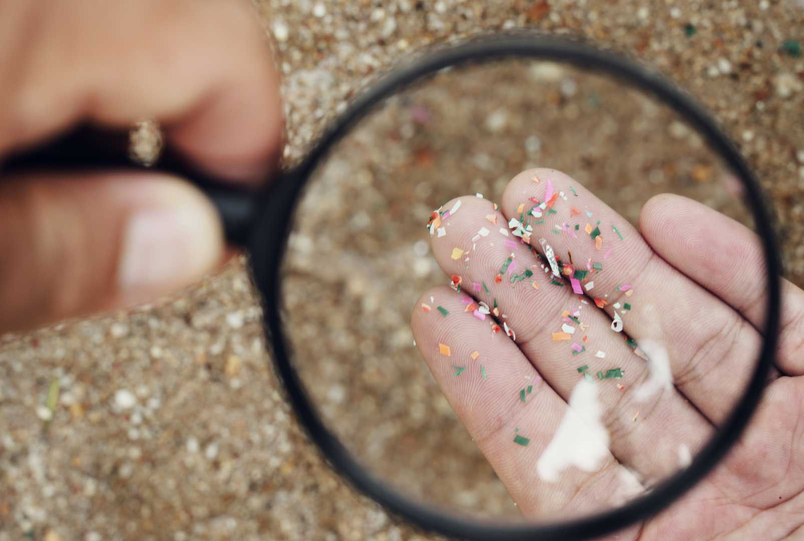 A magnifying glass highlighting small plastic fragments on sand