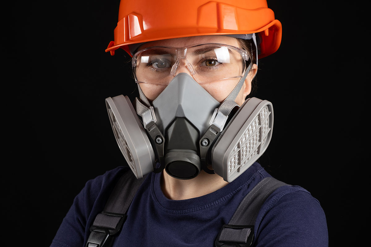 A woman wearing a helmet, respirator and goggles on a black background.