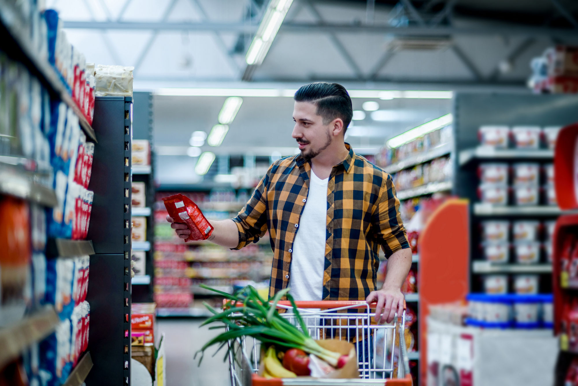 Young handsome man in a supermarket choosing products and holding shopping cart while grocery shopping