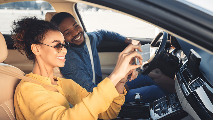 Person in a car using a smartphone in the front passenger seat while the driver operates the vehicle