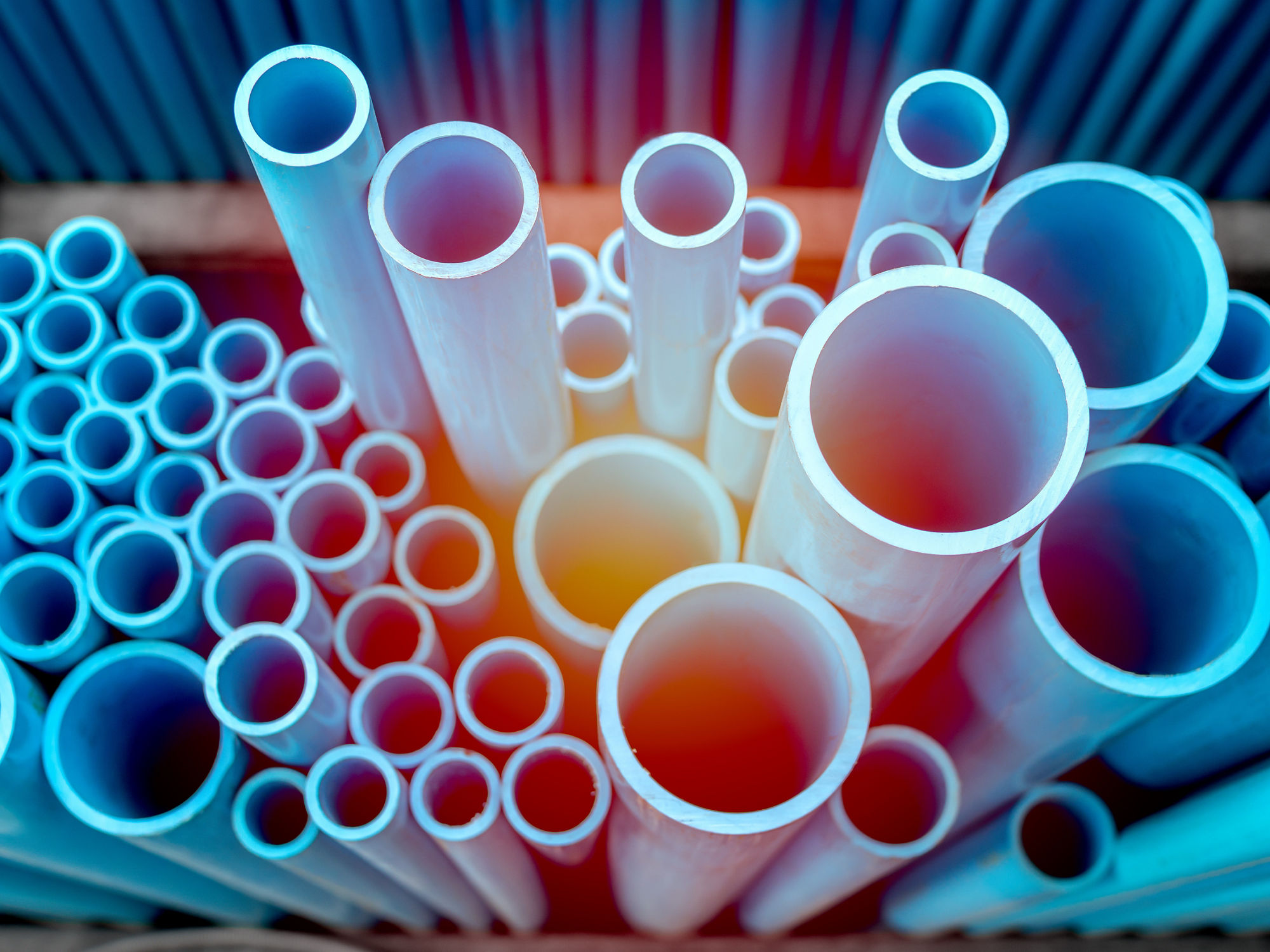 Tubes PVC pipes stacked in warehouse. Blue PVC pipes background with sunlight.