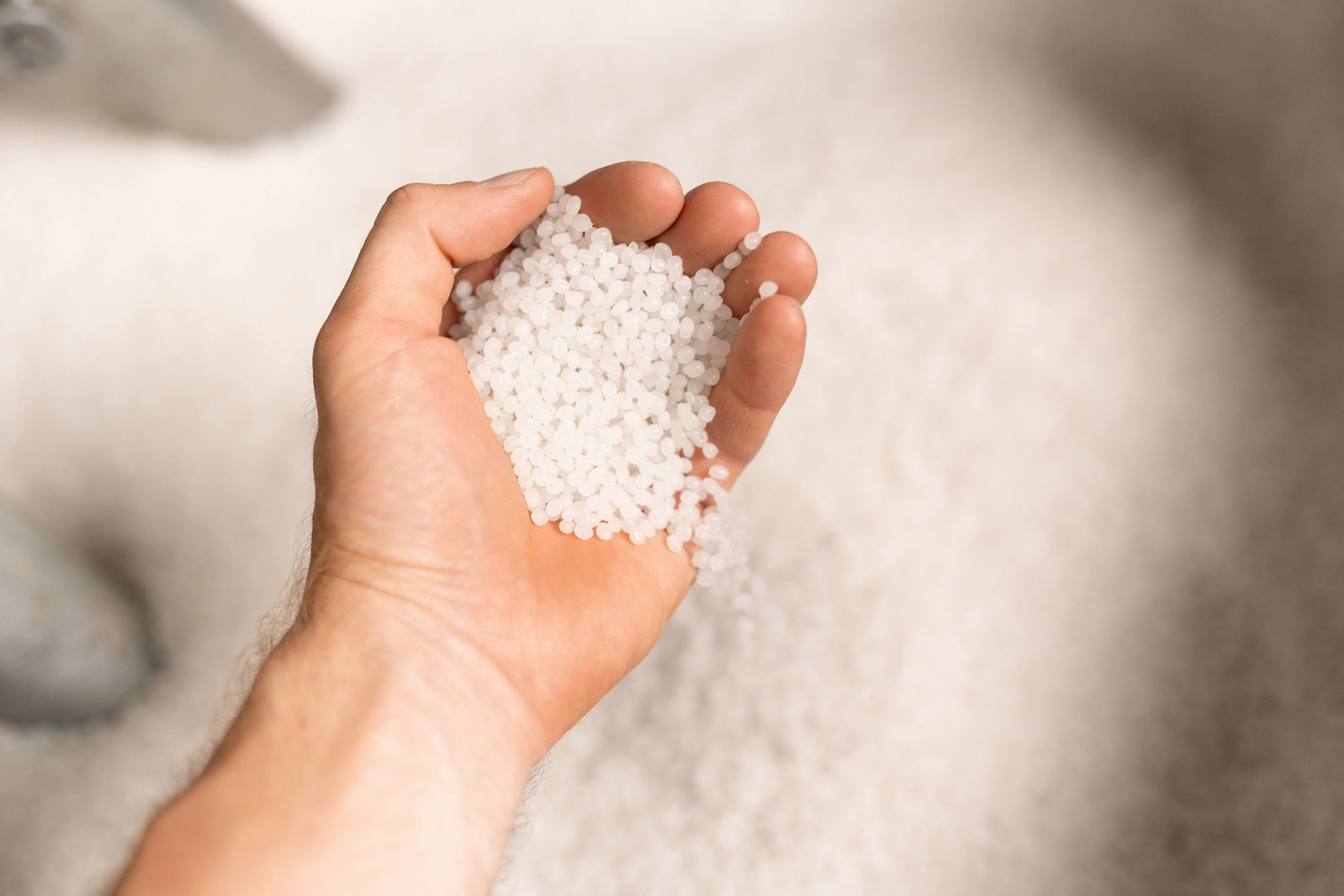 Hand of young male worker of large modern factory holding polymer granules in hand during industrial process