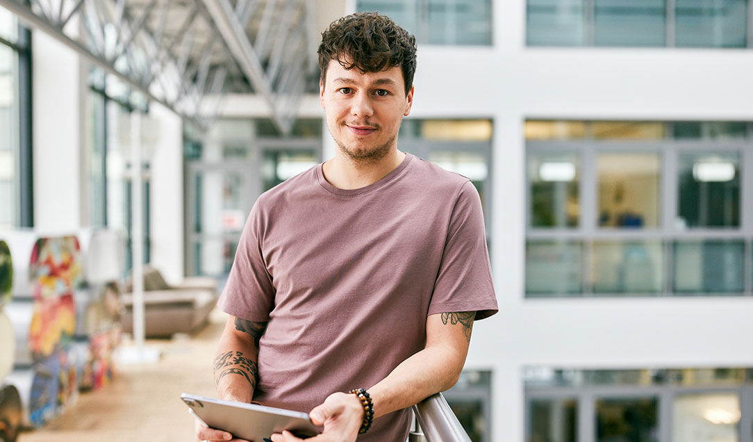 An IT employee stands with a tablet in the office.